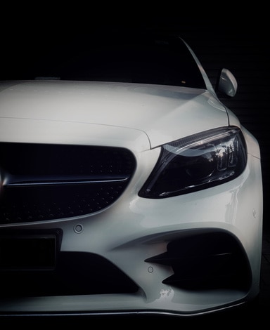 Photo d'une Mercedes blanche vue de face. La moitié droite de la voiture est masquée.